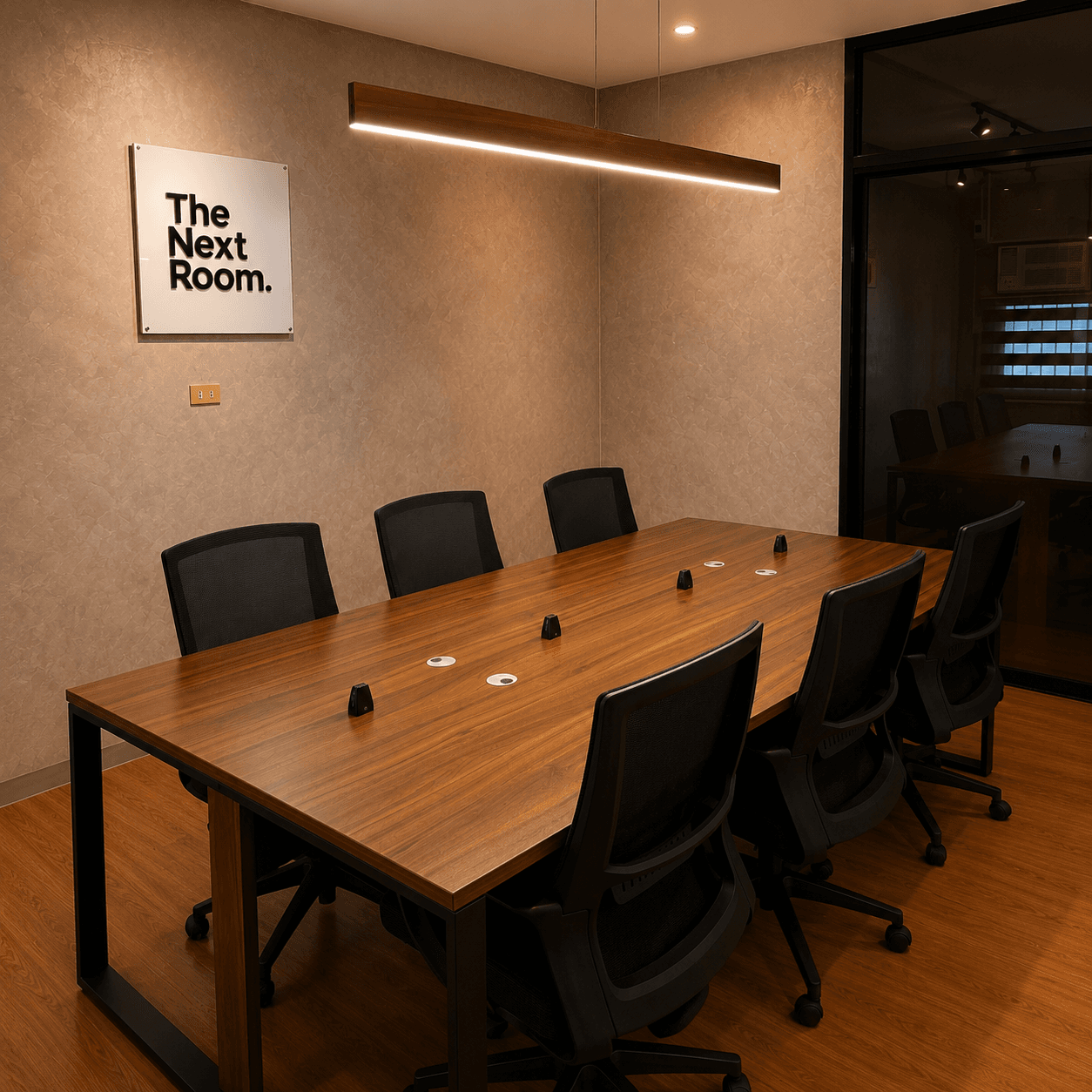 Angled view of The Next Room meeting table, wall sign, and glass partition.